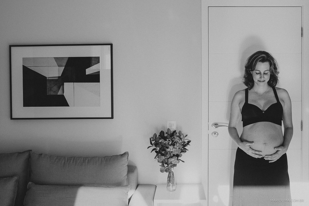 Gravida olhando para a barriga encostada na porta da sala