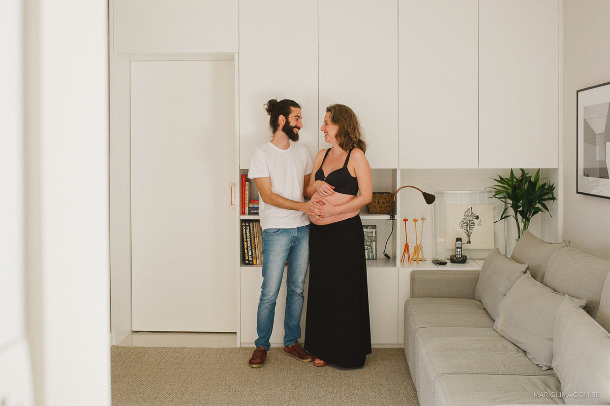 Pais se olhando e acarinhando a barriga na sala de casa