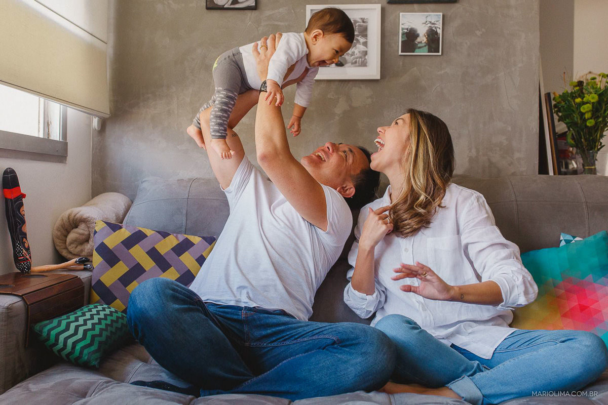 Pais felizes segurando o filho no colo no sofá da sala