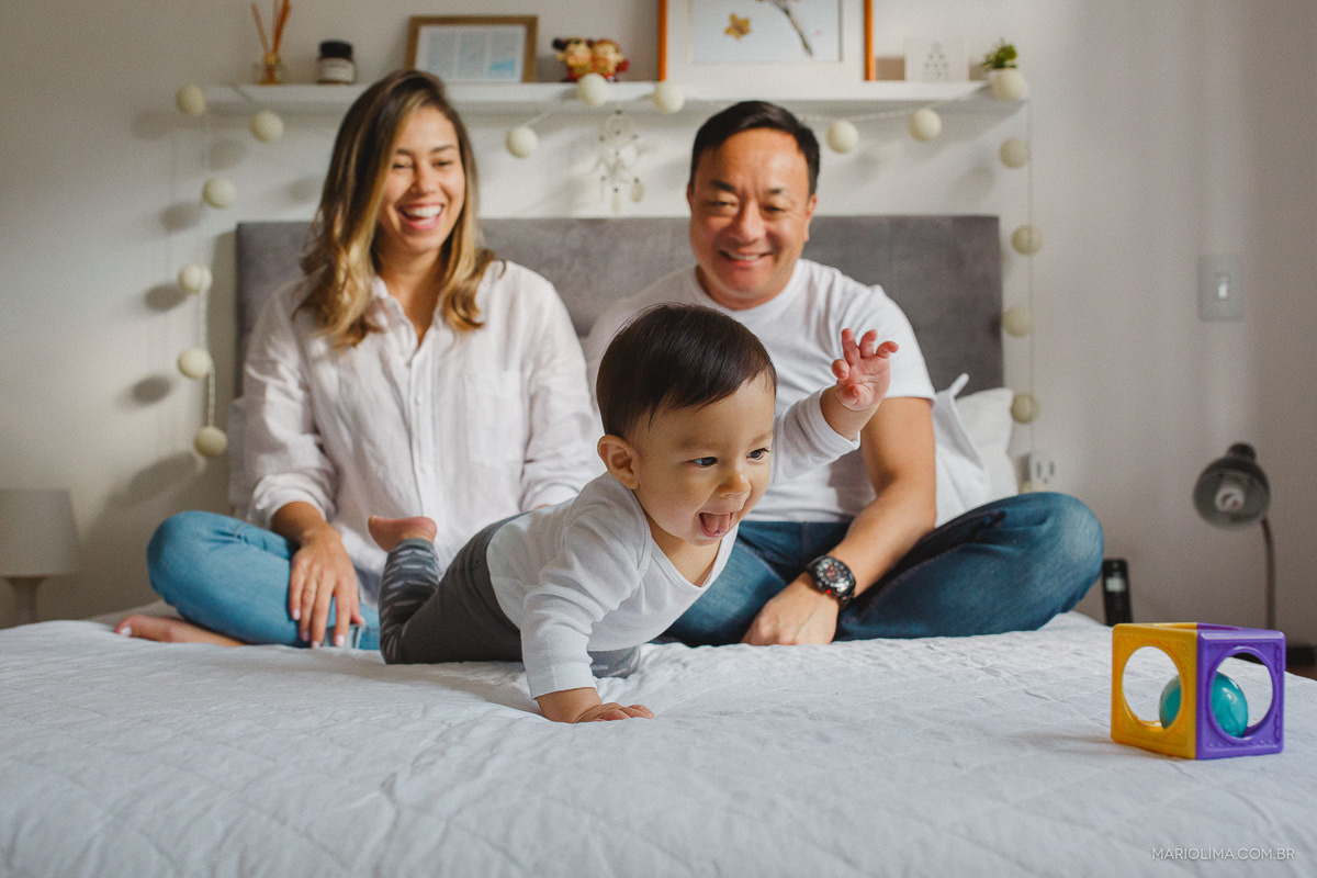 Pais olhando o filho engatinhar na cama atrás de brinquedo