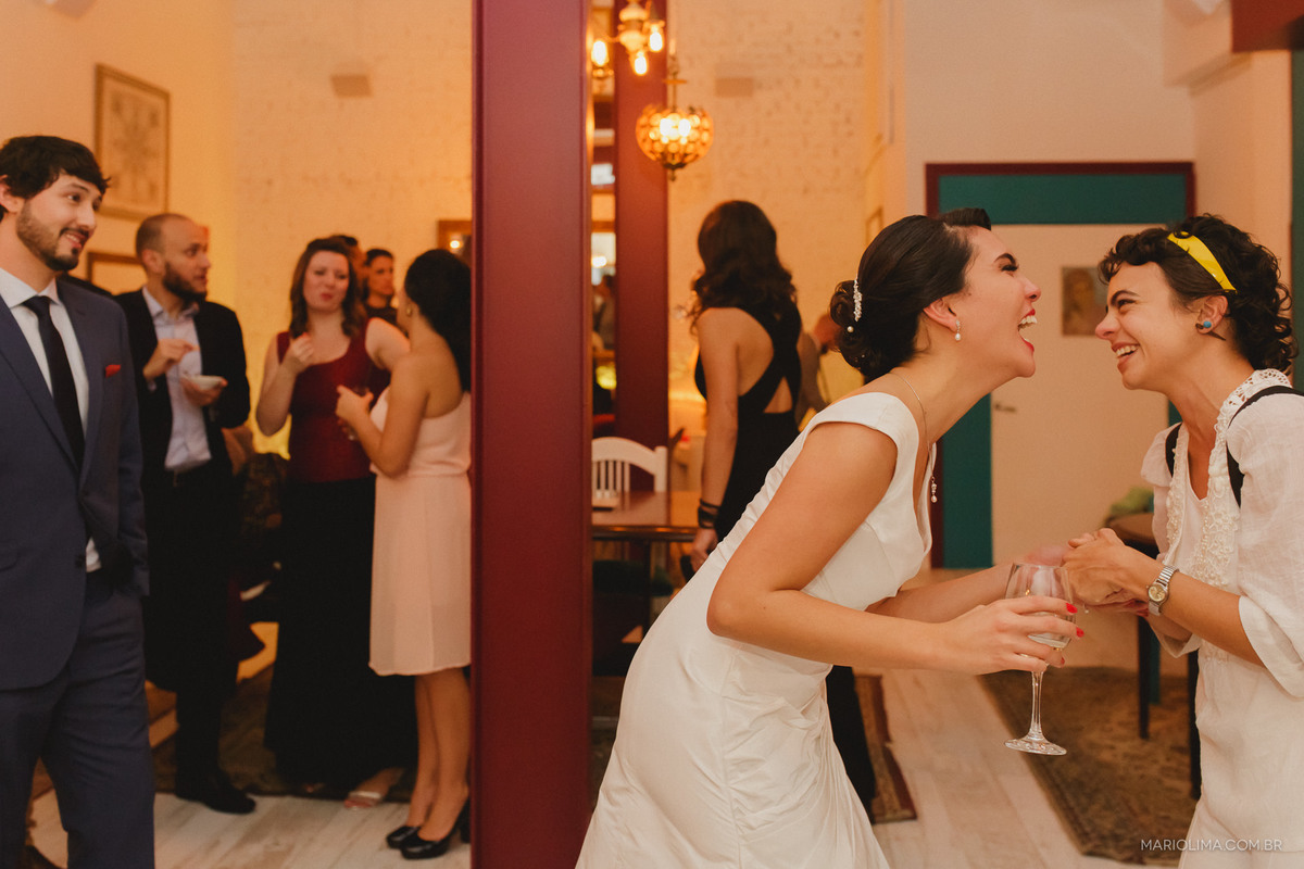 Noivo observando noiva rindo com convidada em frente ao espelho da Casa Marakuthai