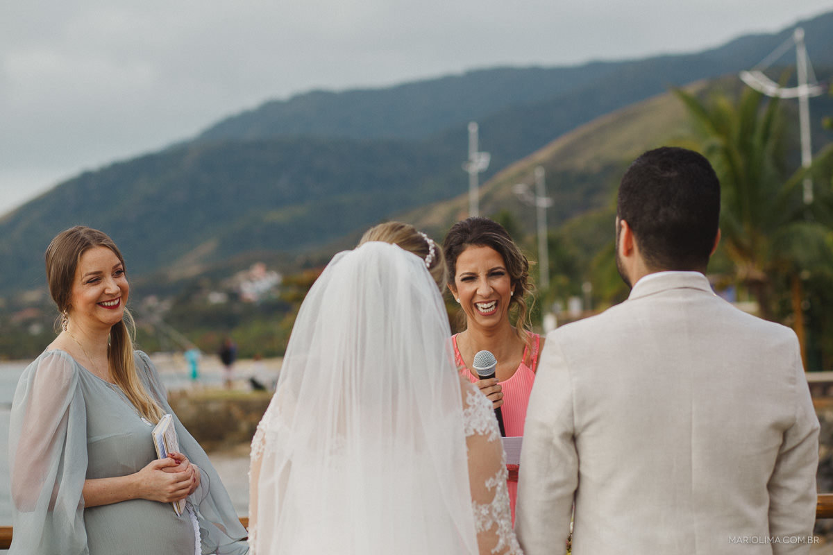 Celebrante olhando para os noivos enquanto irmã faz votos em cerimônia de casamento em Vila das Velas