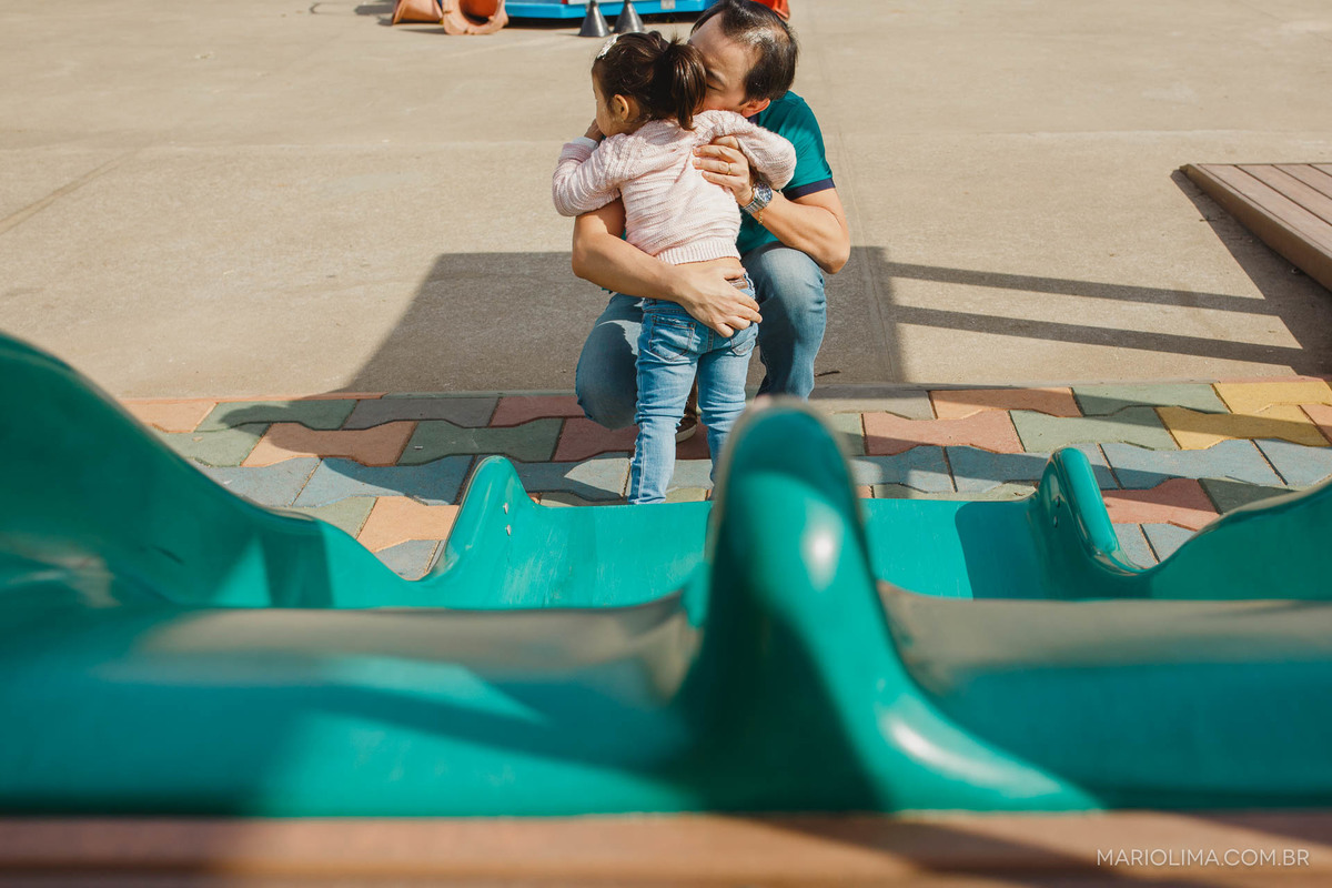 Fotografia de pai abraçando a filha em frente ao escorregador no Parque Villa Lobos