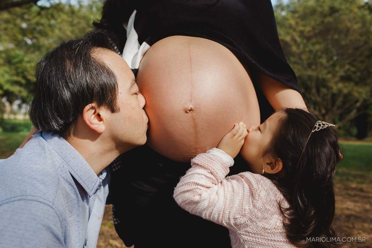 Pai e filha beijando a barriga da mãe em Parque Villa Lobos