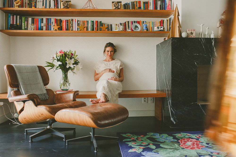 Fotografia de mãe sentada na sala com as mãos na barriga