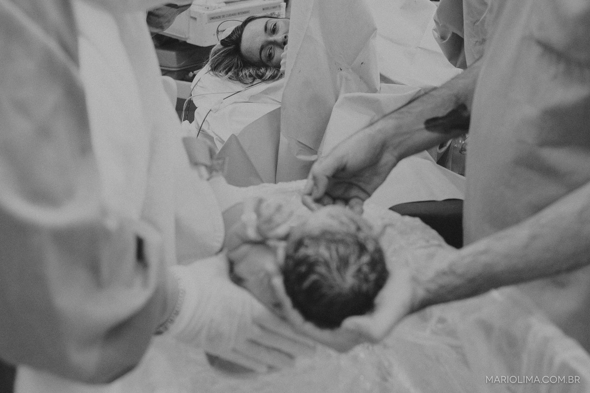 Mãe olhando os médicos cuidarem da neném em sala de parto