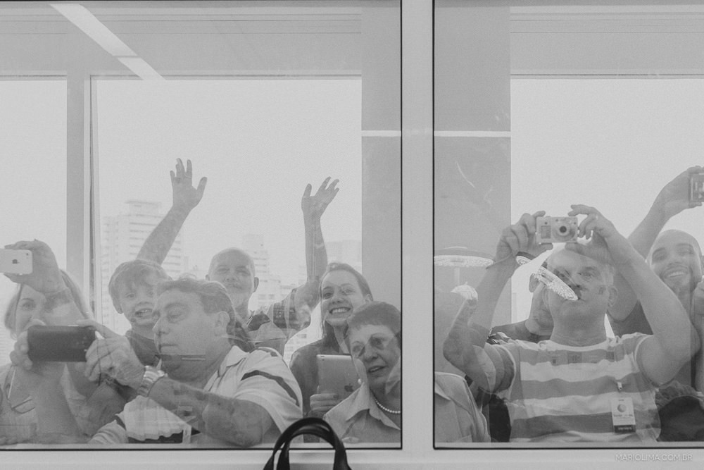 Fotografia de familiares tirando foto da neném atrás do vidro da sala de parto