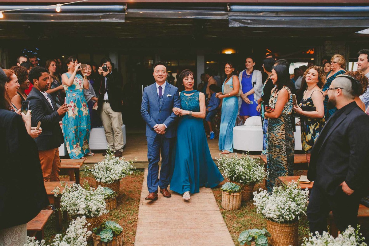 Fotografia de noivo entrando com a mãe em cerimônia de casamento na Casa de Praia em Camburi 