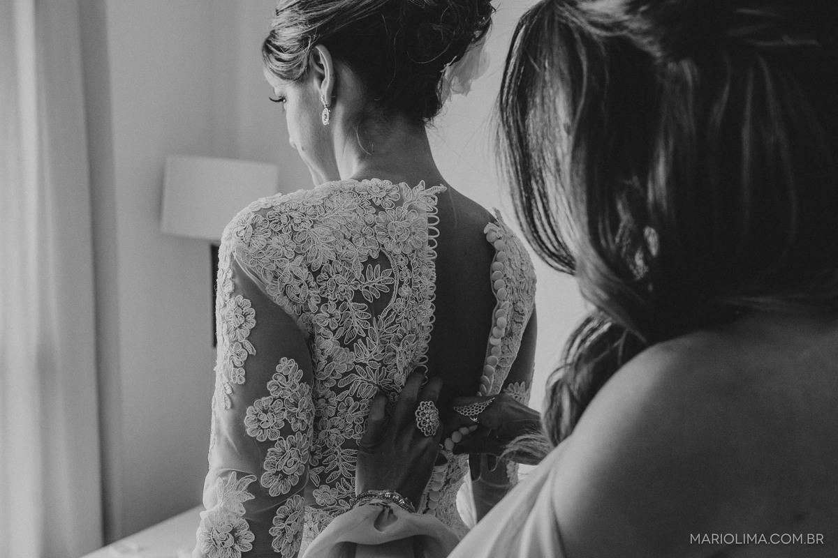 Mãe ajudando a noiva abotoar o vestido no making of