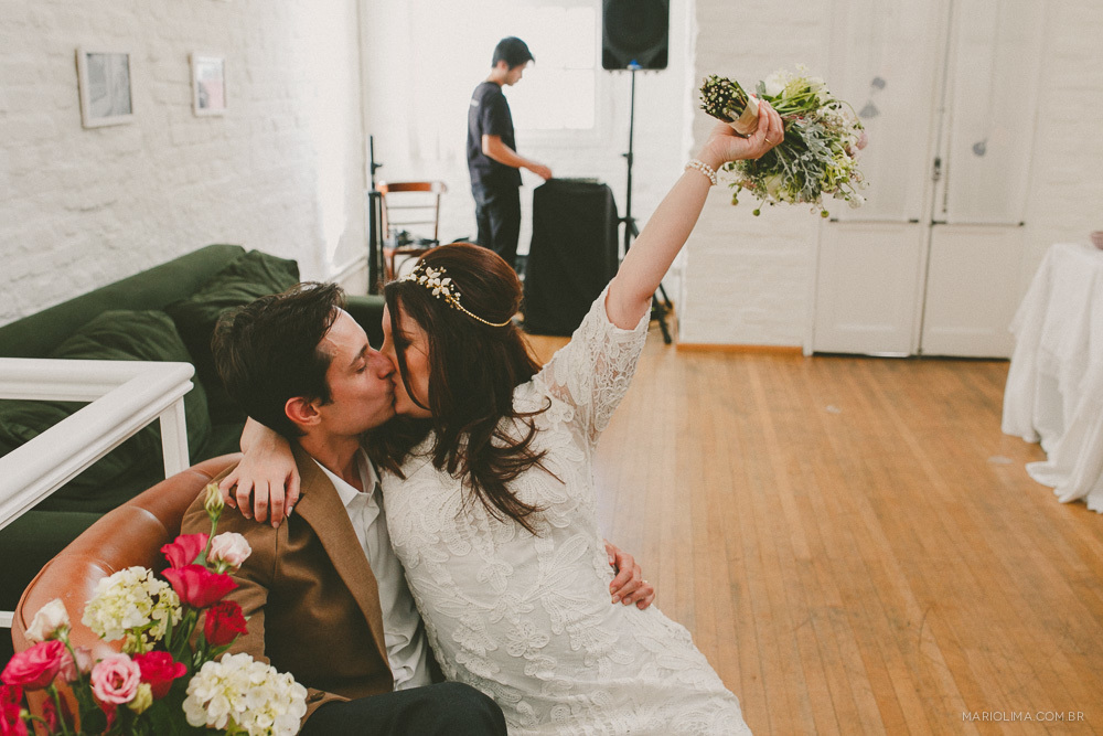 Noiva beijando o noivo e segurando o bouquet para o alto feito por Tais Puntel
