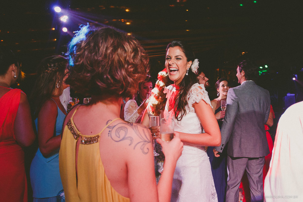 Fotografia de noiva rindo com madrinha em festa de casamento na praia