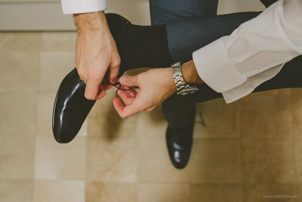 Fotografia de noivo amarrando sapato para cerimônia de casamento 