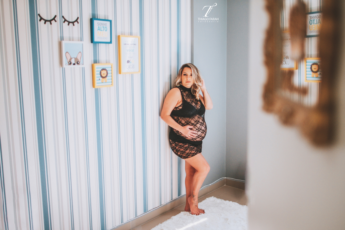 gestante com vestido de renda curto preto transparente, no quarto do bebe, azul e amarelo listrado