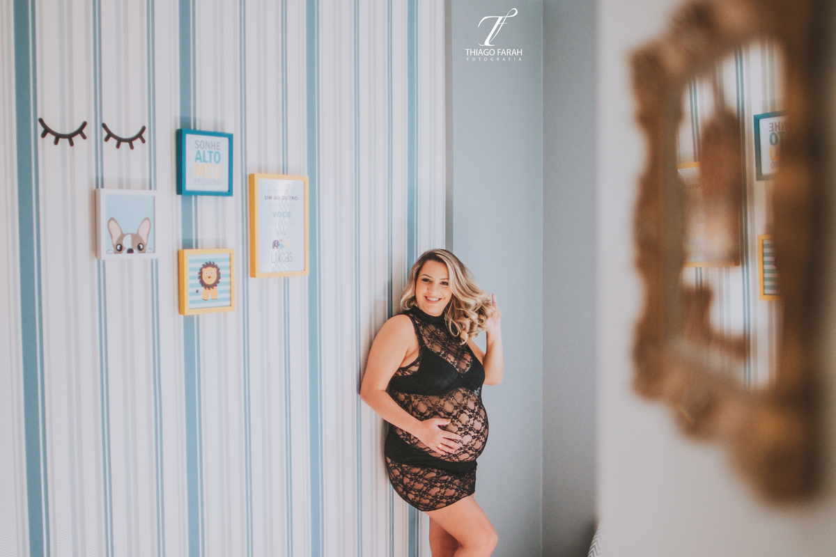 gestante com vestido de renda curto preto transparente, no quarto do bebe, azul e amarelo listrado