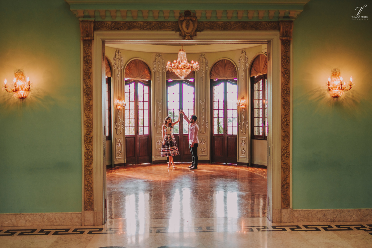 casal dançando no meio da sala, com várias janelas, lustre e arquitetura vitoriana.