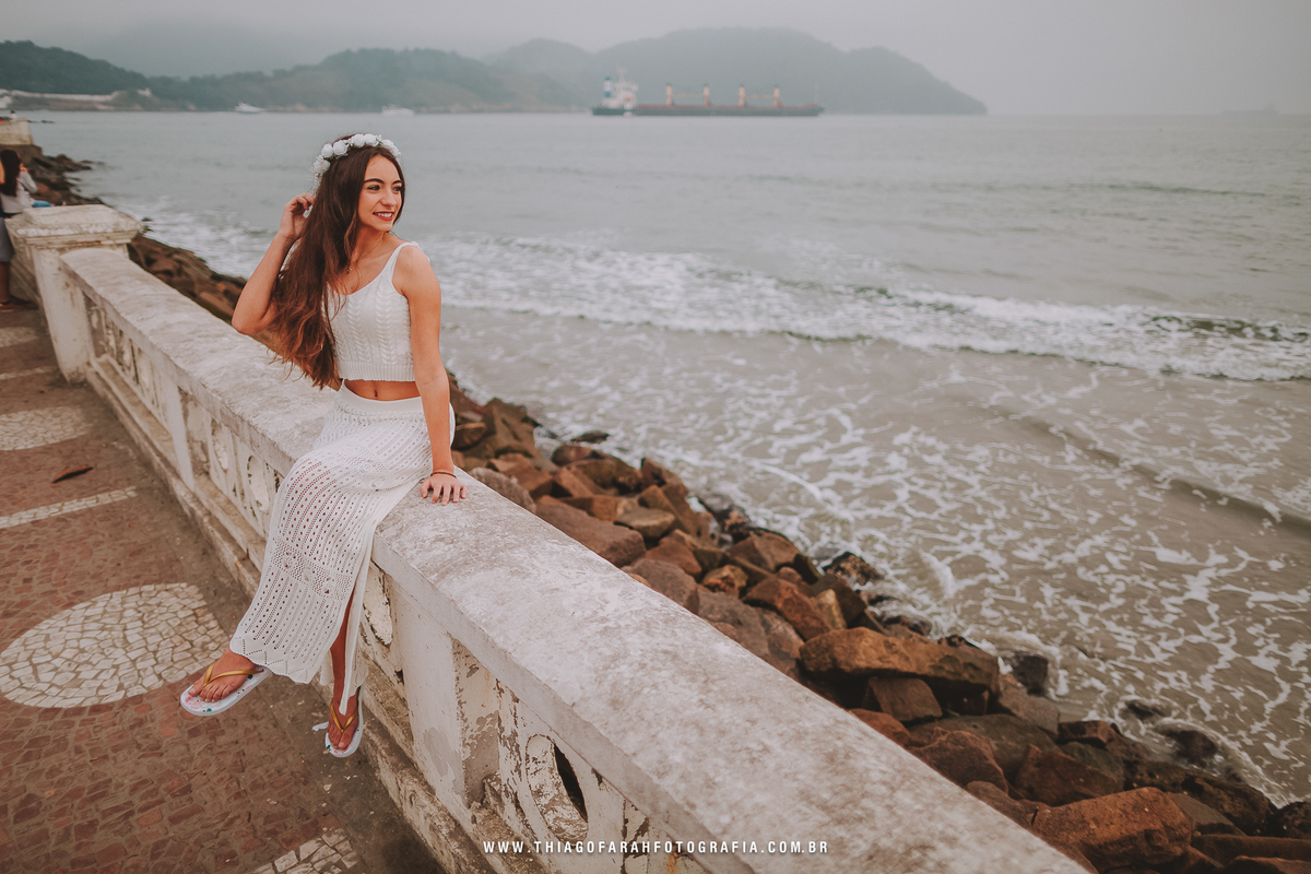 ensaio externo 15 anos em santos, jardim do aquário, ponta da praia, estido branco rendado, coroa de flores, muretas de santos, mar, pedras, nublado