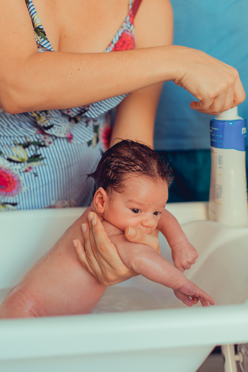 mae lava a cabeça do bebe recem nascido em ensaio fotografico