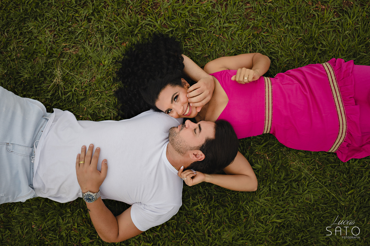 Ensaio fotográfico externo de casal realizado no pesque pague com muito verde. Ensaio externo com pose do casal deitado.