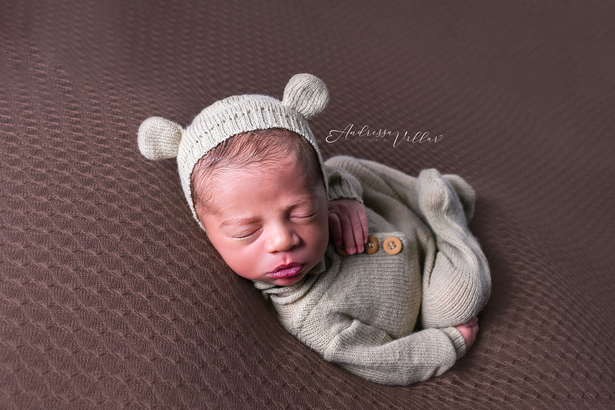 Recém Nascido deitado de barriga para cima com touca de ursinho da cor do macacão (bege)