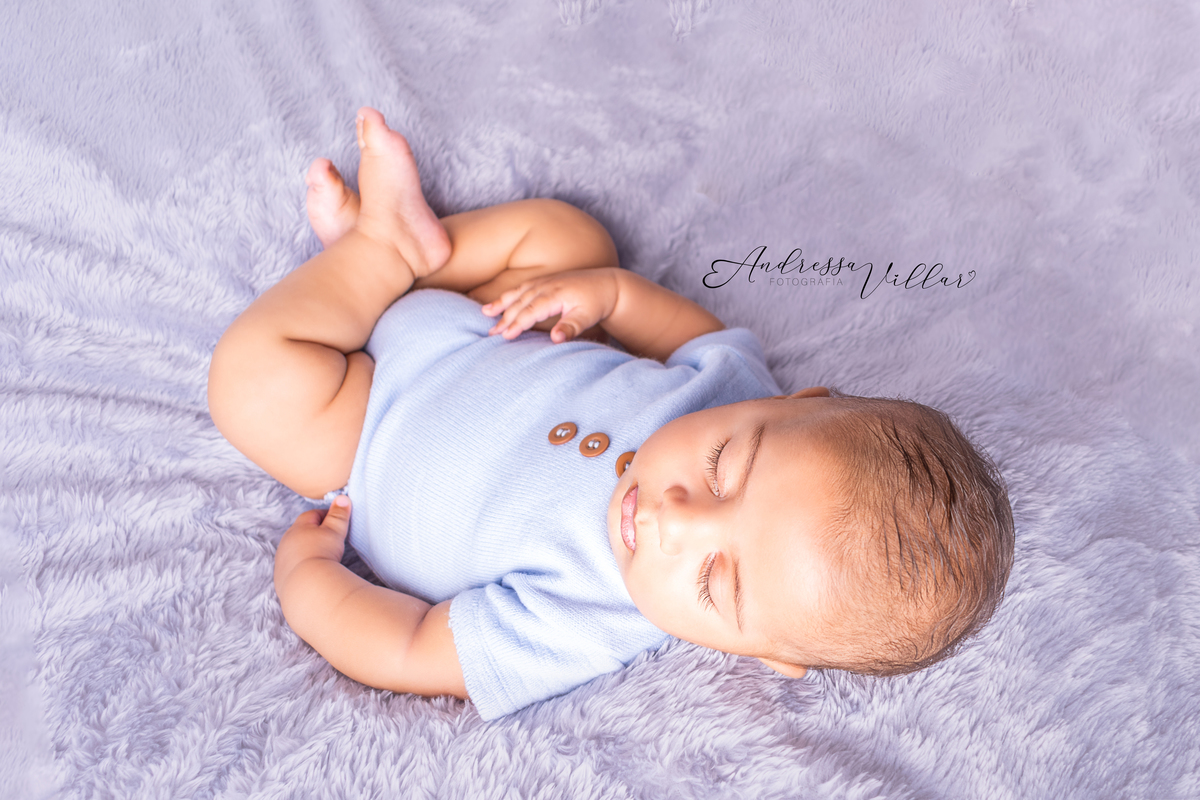 Gustavo 3 meses dormindo de barriga para cima com body azul claro 
