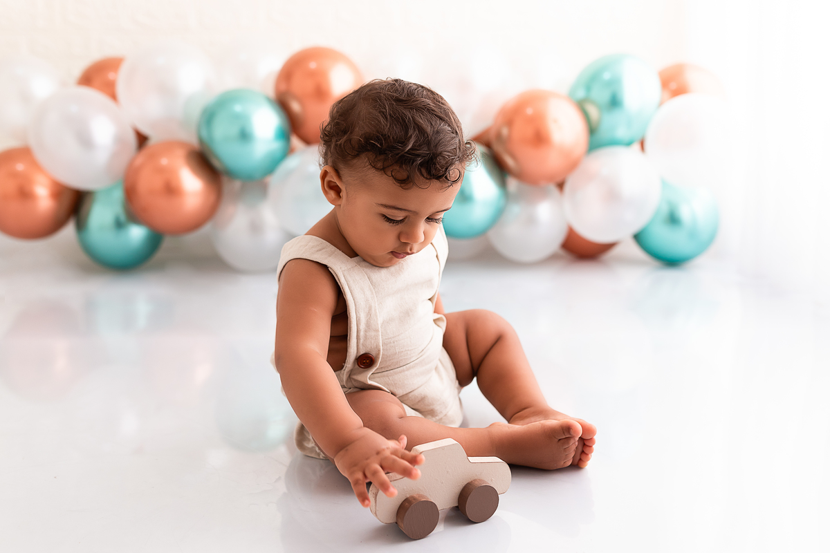 Bebê brincando de carrinho com balões no fundo