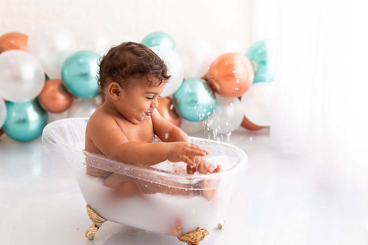 bebê na banheira tomando banho de leite e jogando água pro alto