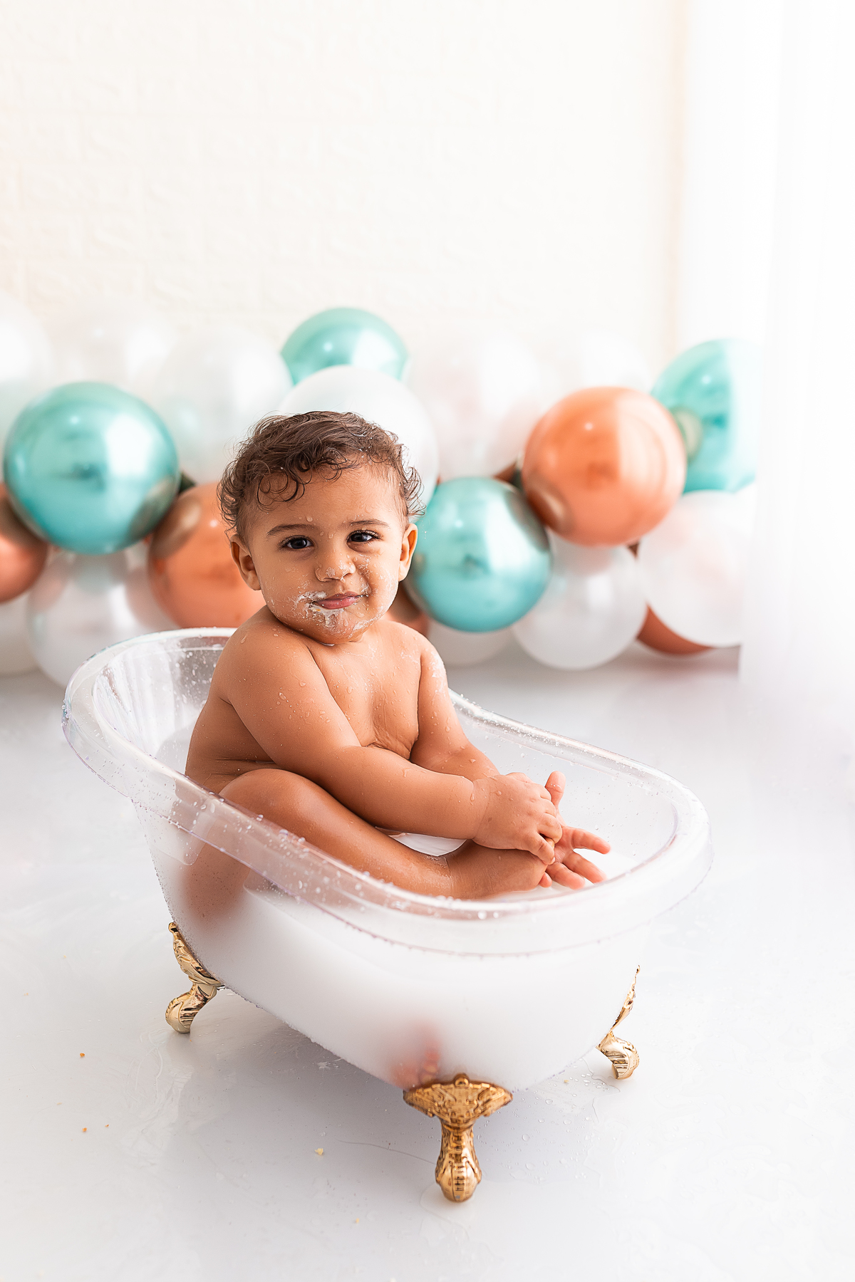 bebê na banheira tomando banho de leite e balões ao fundo