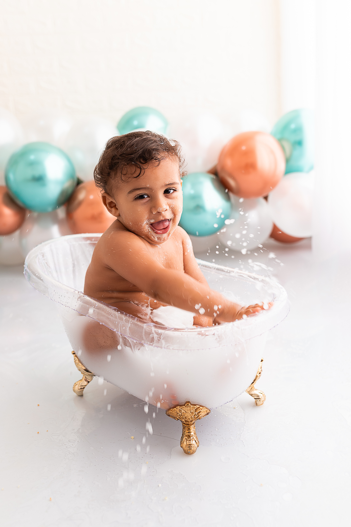 bebê na banheira tomando banho de leite e jogando água pro alto