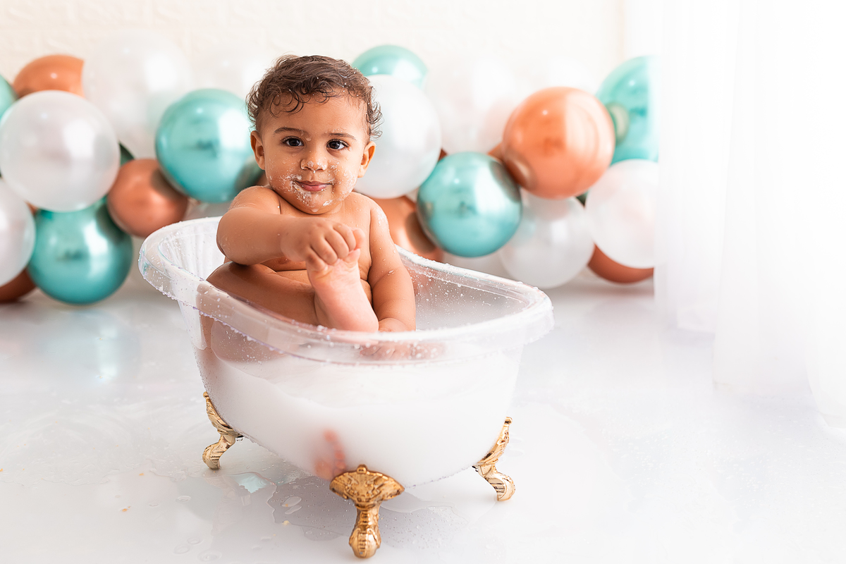 bebê na banheira tomando banho de leite e segurando o pé