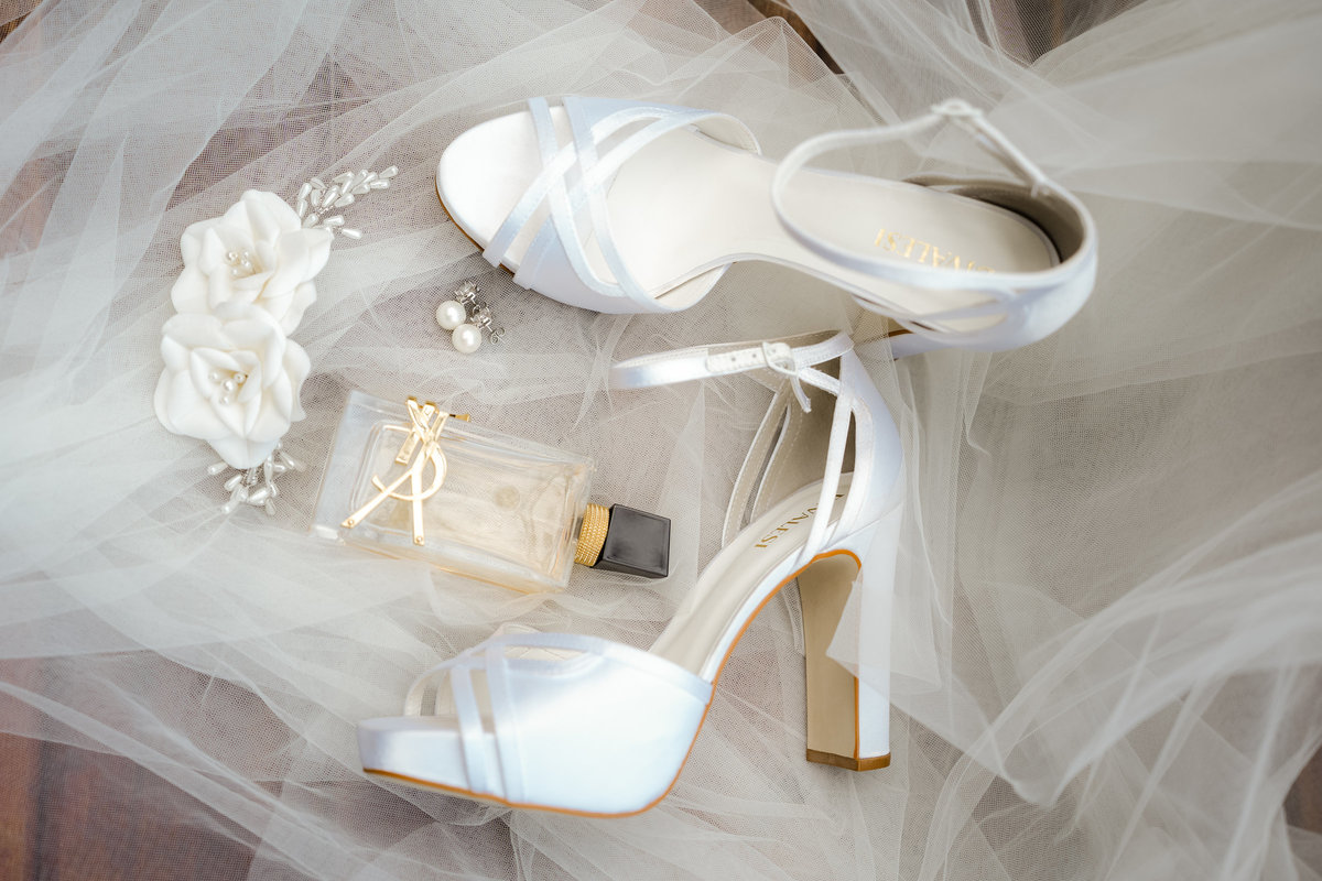 Sapatos brancos, perfume e acessórios da noiva organizados delicadamente sobre o véu, durante os preparativos do casamento de Ana Rute.