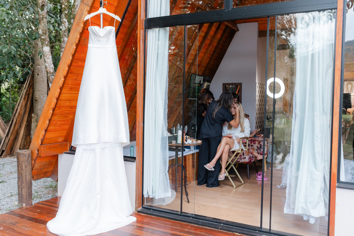 Vestido de noiva pendurado junto à entrada de uma construção de madeira, durante os preparativos para o casamento no Sítio Santa Paula.