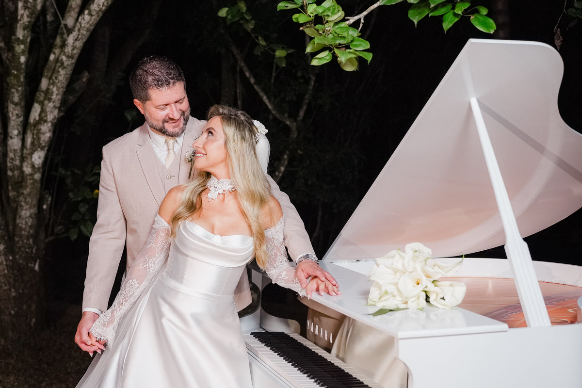 Um momento de cumplicidade entre Ana Rute e Juliano junto ao piano branco durante a recepção do casamento.