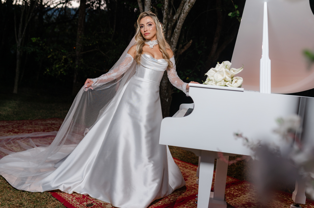 A elegância de Ana Rute em um retrato noturno junto ao piano branco no Sítio Santa Paula.