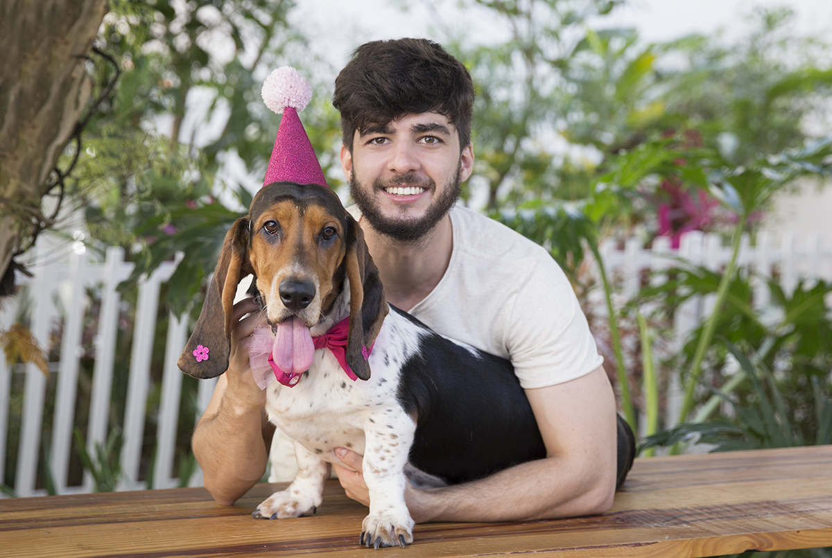 Basset Hound posando com seu chapeu de aniversario no jardim, junto com o tutor