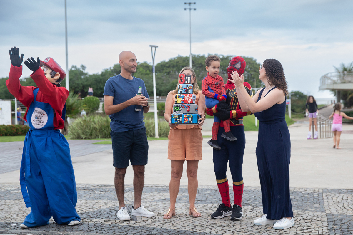 Aniversariante, junto com vovó, papai, mamãe, Homem-aranha e Mario Brós, cantando parabéns na orla de Camburi 