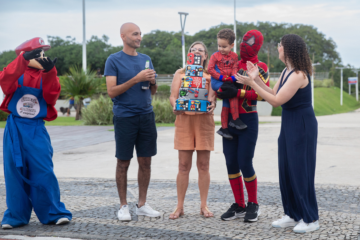 Aniversariante, junto com vovó, papai, mamãe, Homem-aranha e Mario Brós, cantando parabéns na orla de Camburi 