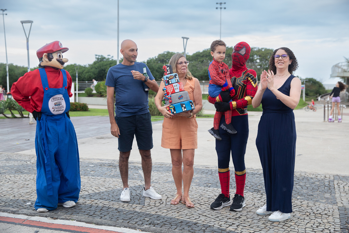 Aniversariante, junto com vovó, papai, mamãe, Homem-aranha e Mario Brós, cantando parabéns na orla de Camburi 