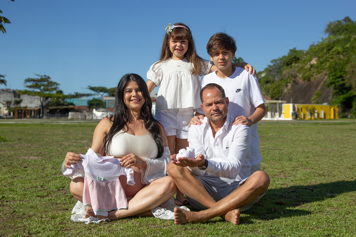 família sentada lado a lado, com destaque para roupinha da bebê que vai chegar 