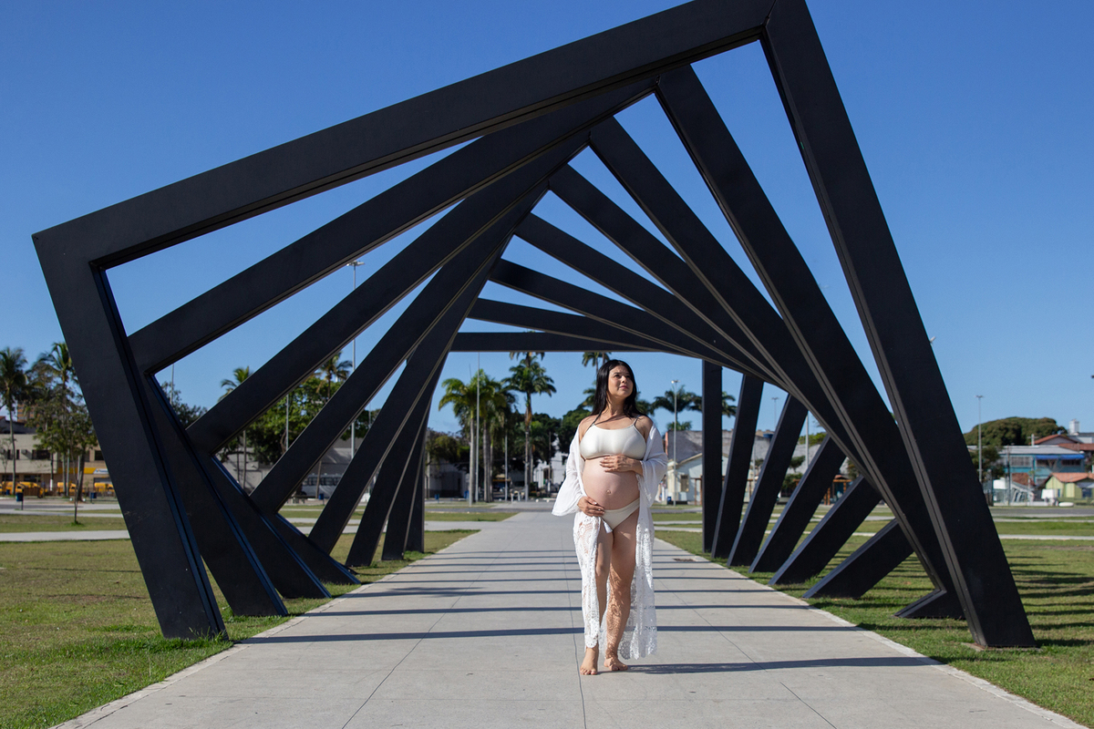 Gestante posa para foto, com as mãos na barriga. em frente ao monumento do parque