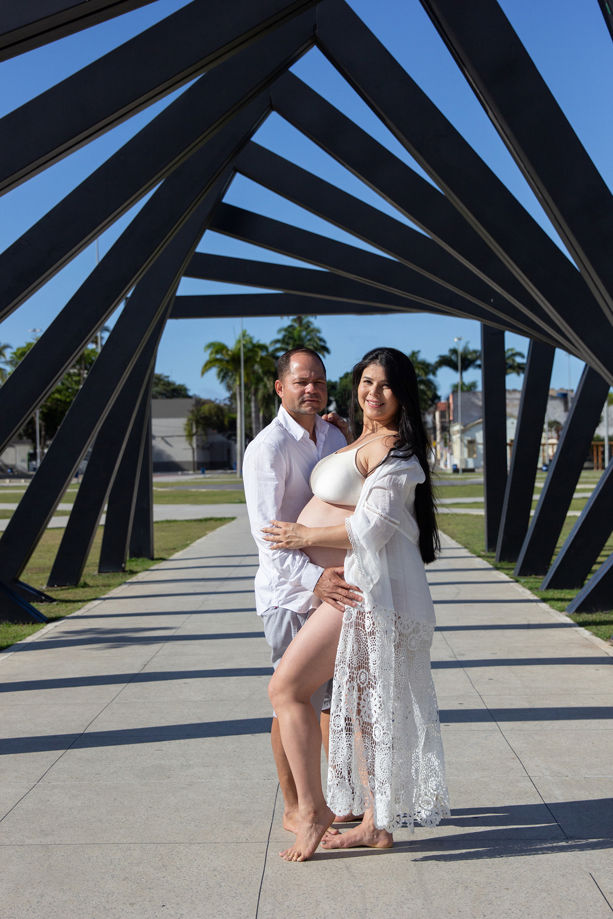 casal posa para foto, com as mãos na barriga. em frente ao monumento do parque