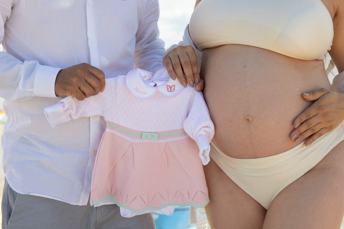 fotos da barriga e mãos do casal, segurando roupinha da bebê que vai chegar