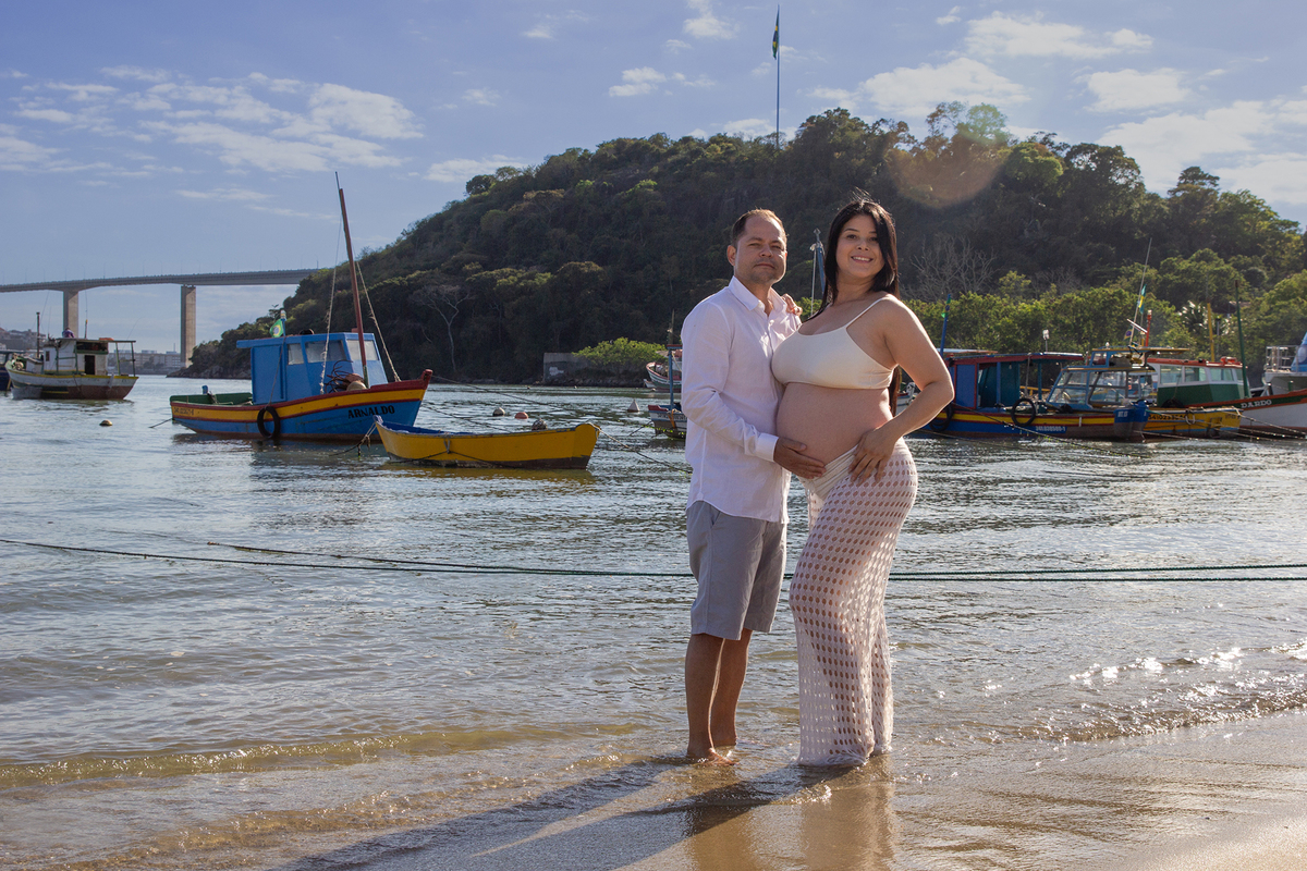 casal, posando para foto, na praia, com mar e terceira ponte ao fundo 