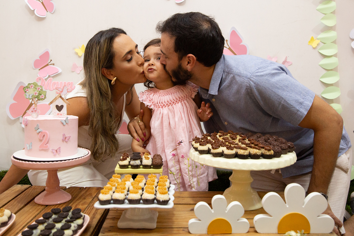 Papai e mamãe dando beijo na aniversariante, na mesa do bolo, em aniversario intimista