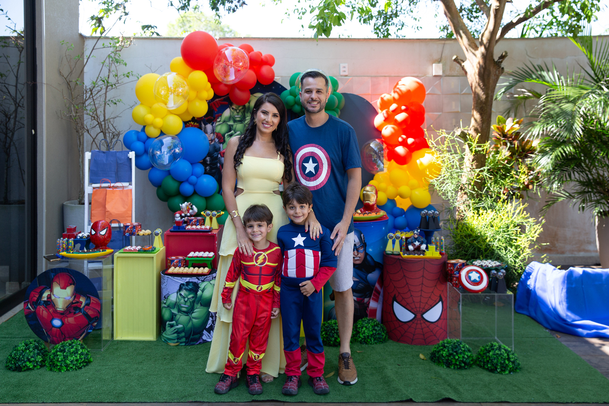 Família posando durante festa de aniversário com tema heróis, rodeada de amigos fantasiados