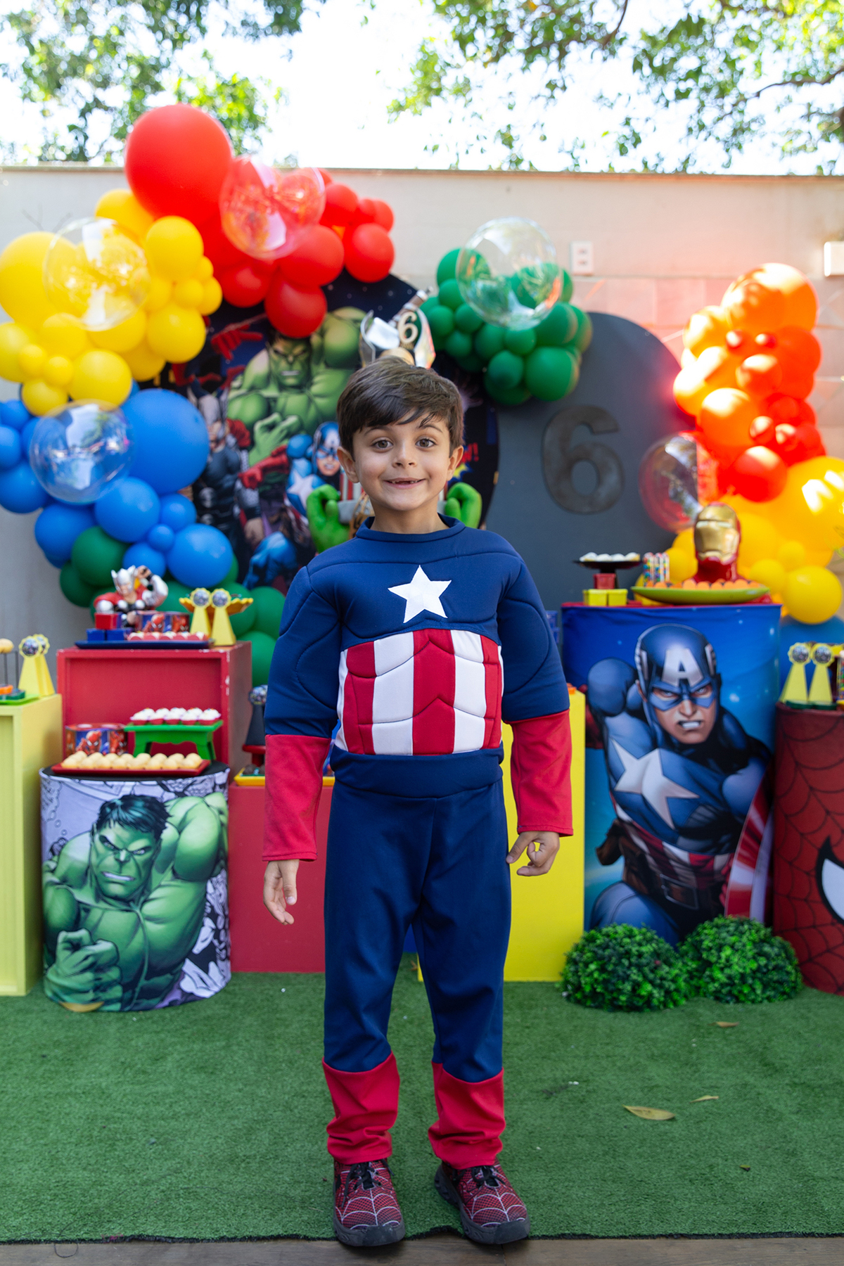 aniversariante, vestido de capitão américa, posando em frente a decoração do aniversario 