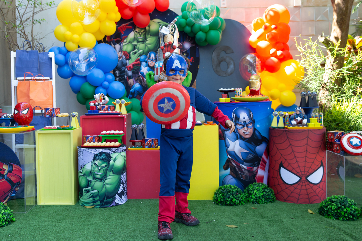aniversariante, vestido de capitão américa, posando em frente a decoração do aniversario 