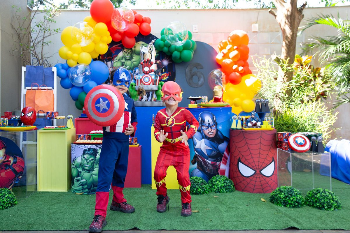 aniversariante e irmão, vestidos de capitão américa e flash, posando em frente a decoração do aniversario 