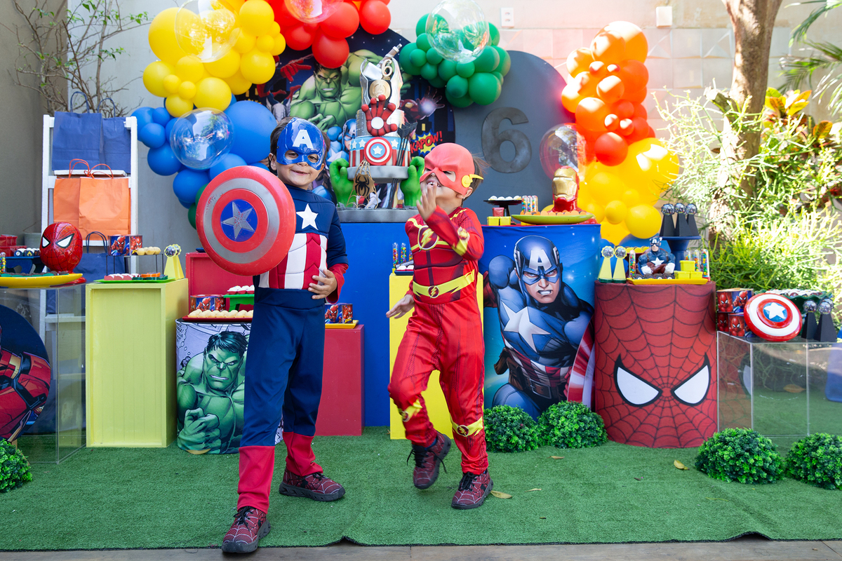 aniversariante e irmão, vestidos de capitão américa e flash, posando em frente a decoração do aniversario 