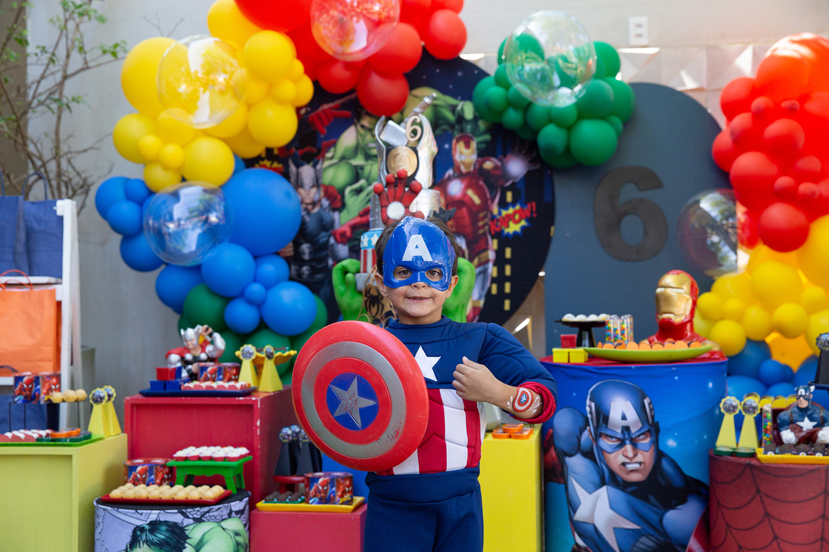aniversariante, vestido de capitão américa, posando em frente a decoração do aniversario 