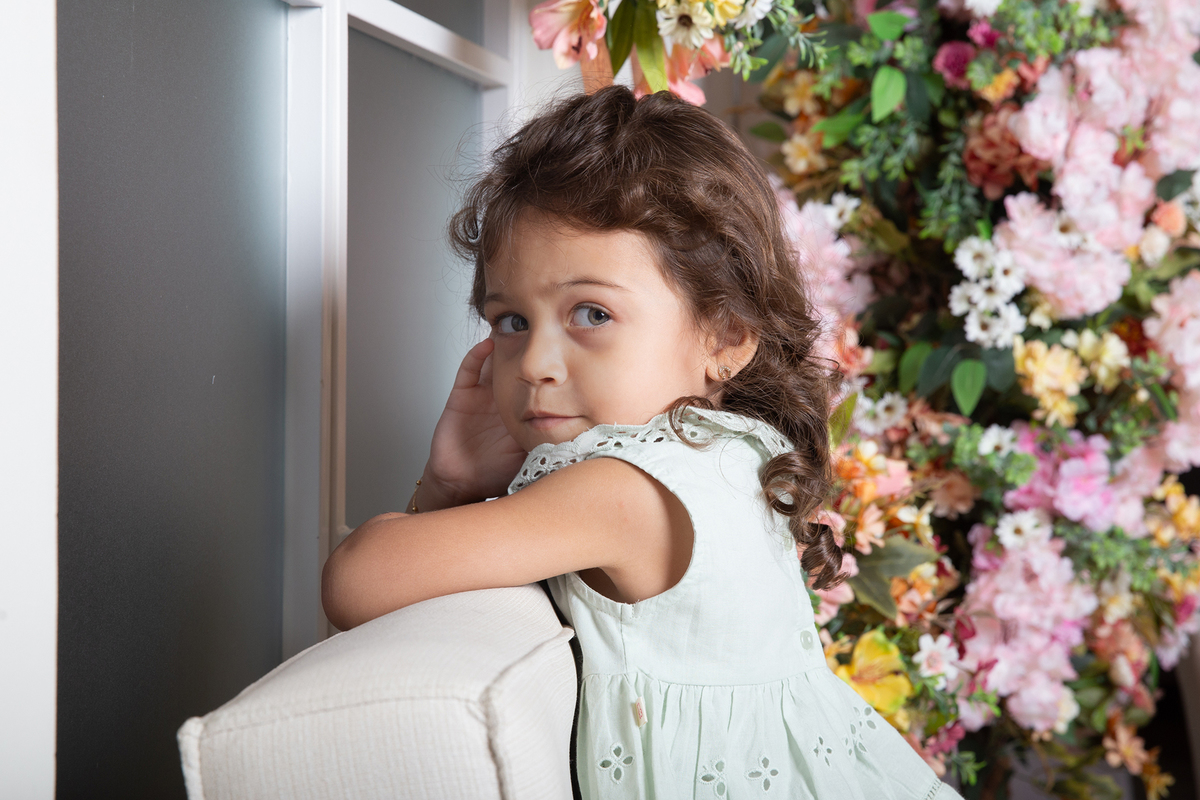 Filha posa para foto no sofá do estúdio, decorado com flores